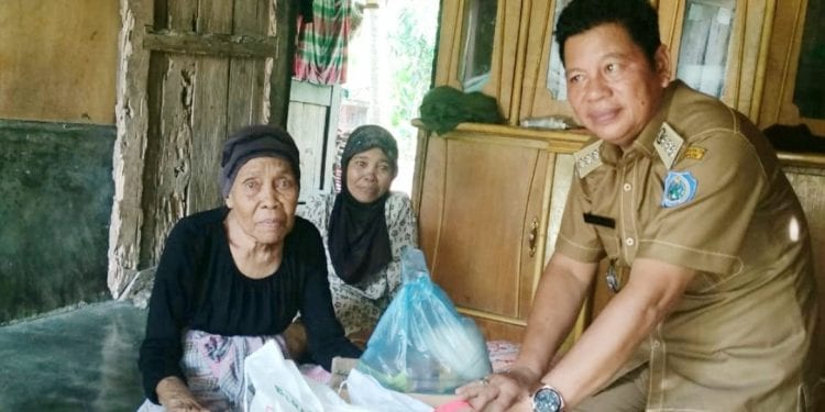 Camat Rantau Utara Turing Ritonga saat menyerahkan bantuan berupa sembako kepada Nek Masniar, warga Kelurahan Pulo Padang.