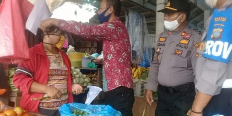 Plt Kadis Perindag Labuhanbatu saat memakaikan masker kepada salahseorang pedagang di pasar Ajamu.